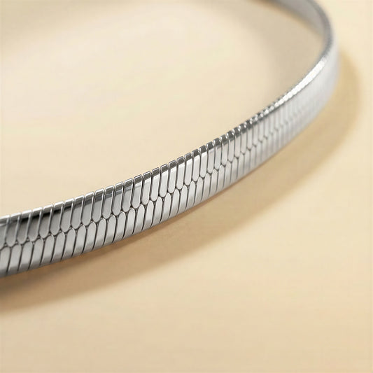 A close-up of a silver snake skin chain bracelet on a warm beige background.