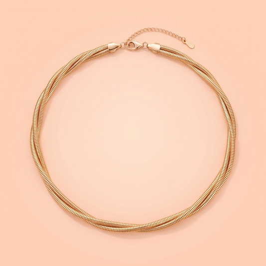Treccia Choker in gold laid flat on a peach background