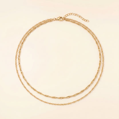 A delicate double-layered gold chain necklace with a small lobster clasp and extender chain, displayed on a light cream background.