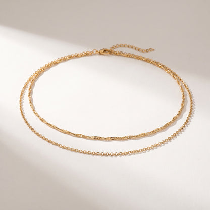 A delicate gold double-layer necklace with a twisted top chain and a fine beaded bottom chain, displayed on a clean white surface with soft shadows.