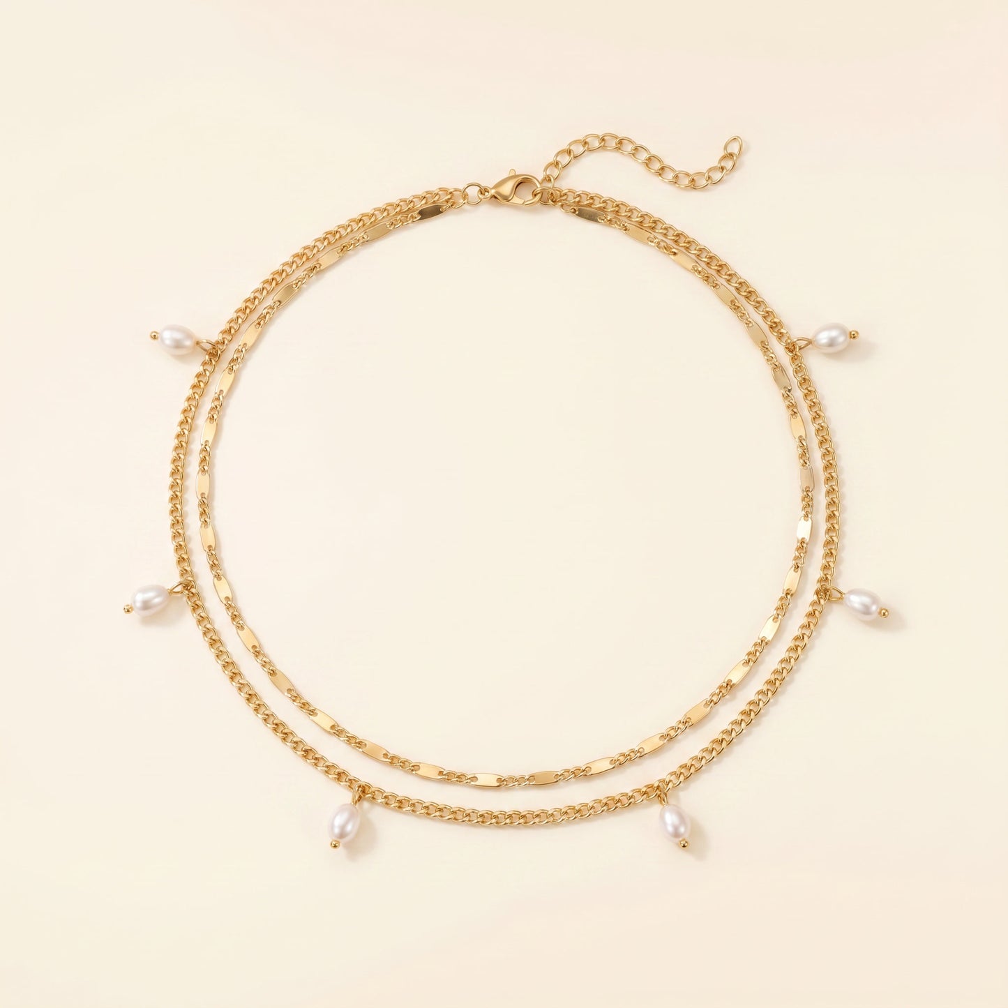 A gold-toned double-strand chain necklace with small dangling white pearl beads, displayed on a light cream background.