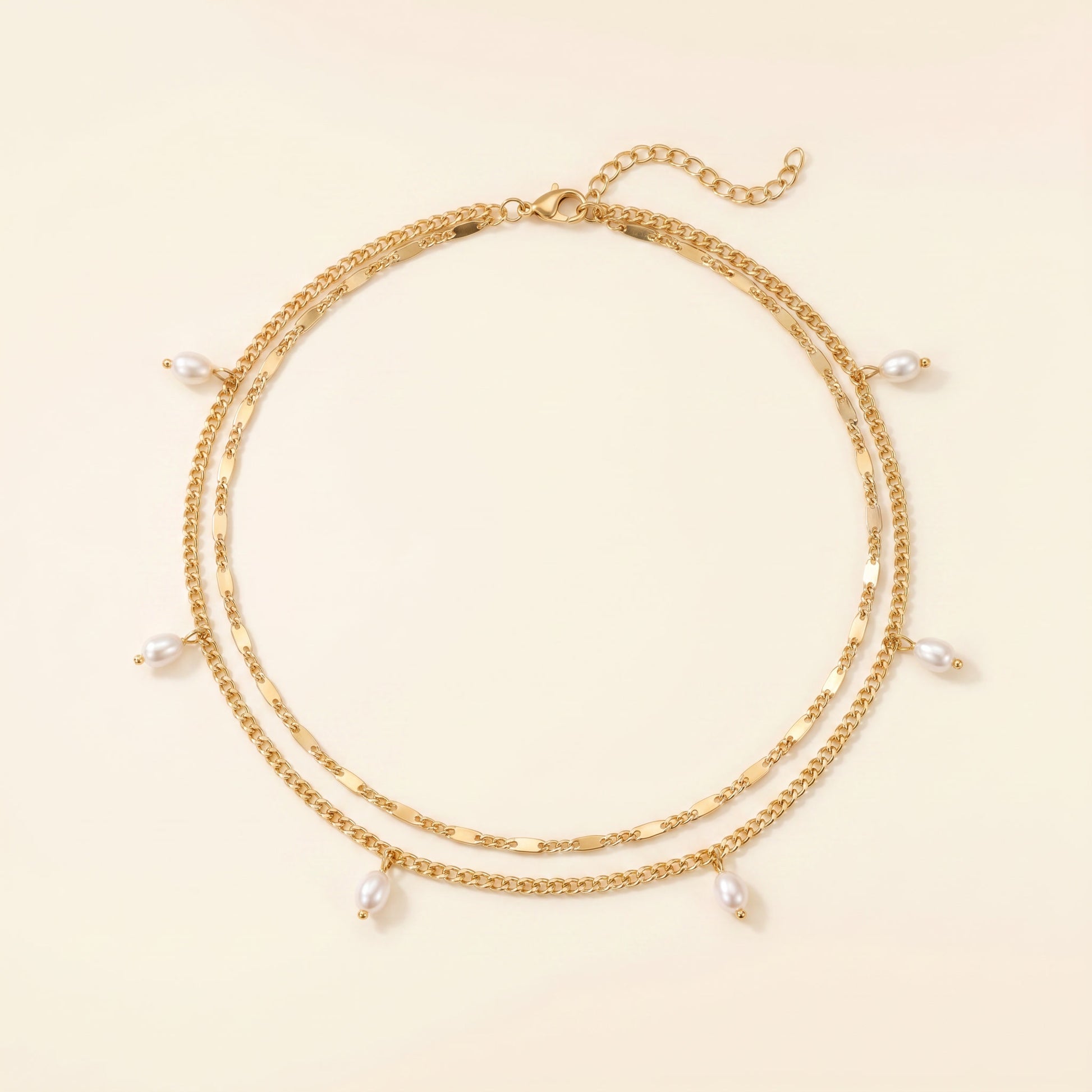 A gold-toned double-strand chain necklace with small dangling white pearl beads, displayed on a light cream background.
