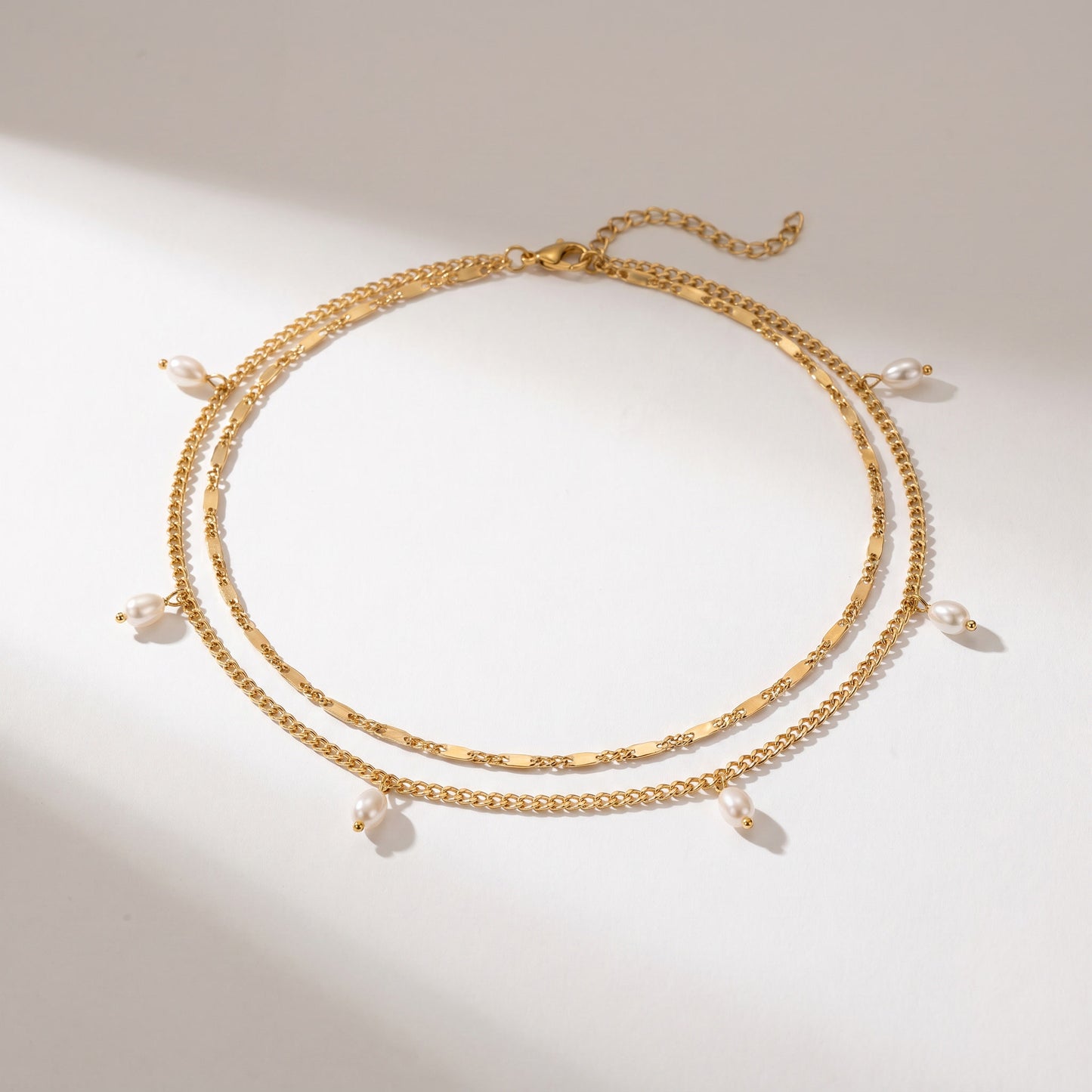 A gold-toned double-strand chain necklace with small dangling pearl beads, displayed on a clean white surface with soft shadows.