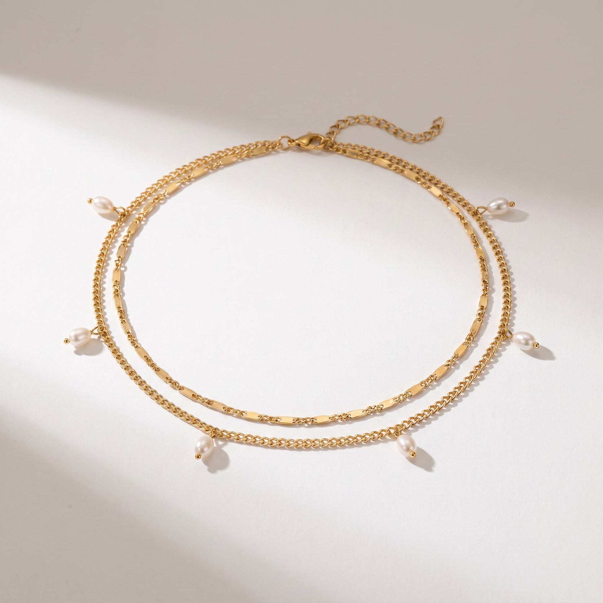 A gold-toned double-strand chain necklace with small dangling pearl beads, displayed on a clean white surface with soft shadows.