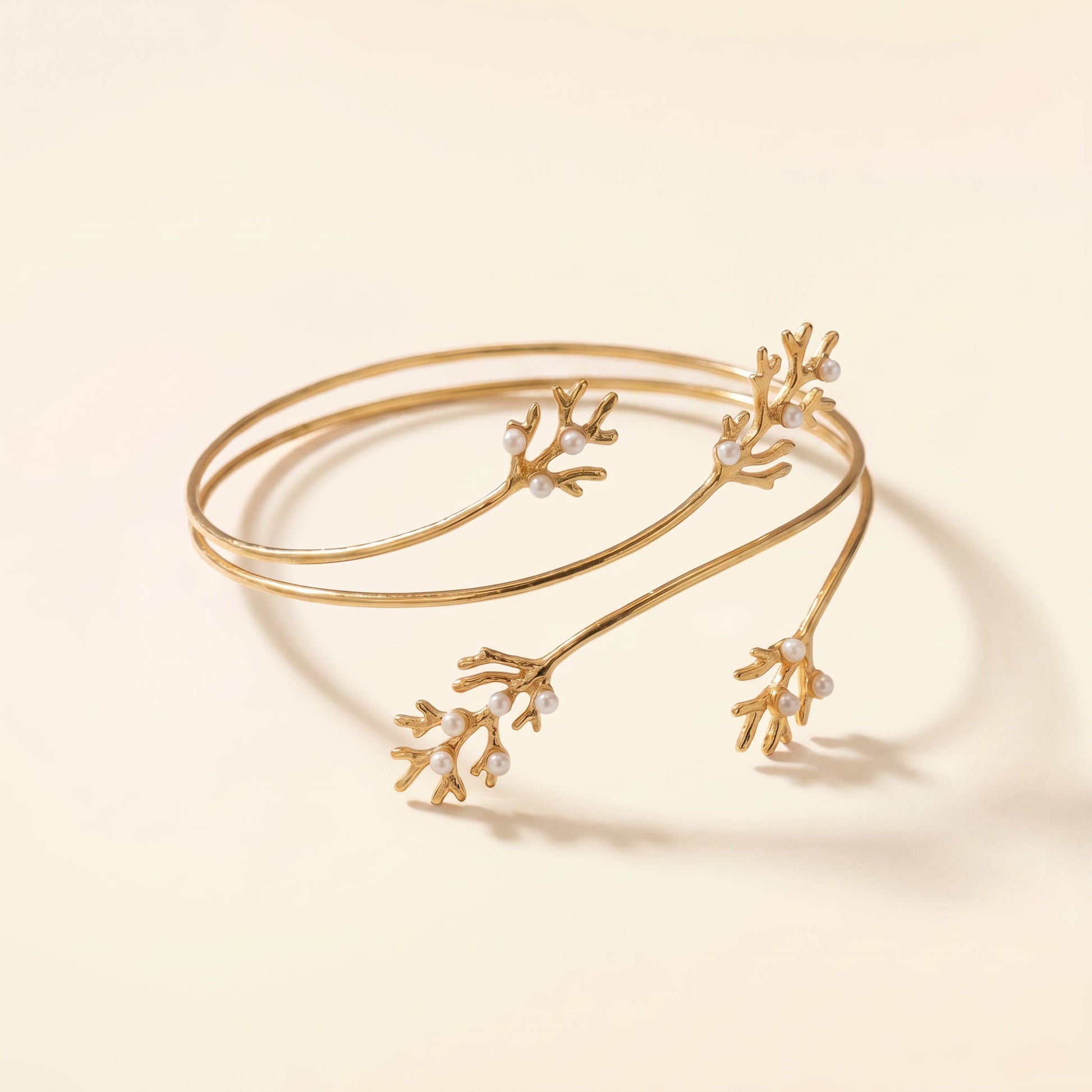 A delicate gold open cuff bracelet designed to resemble coral or branch-like structures, embellished with small clear stones, photographed on a warm cream background.