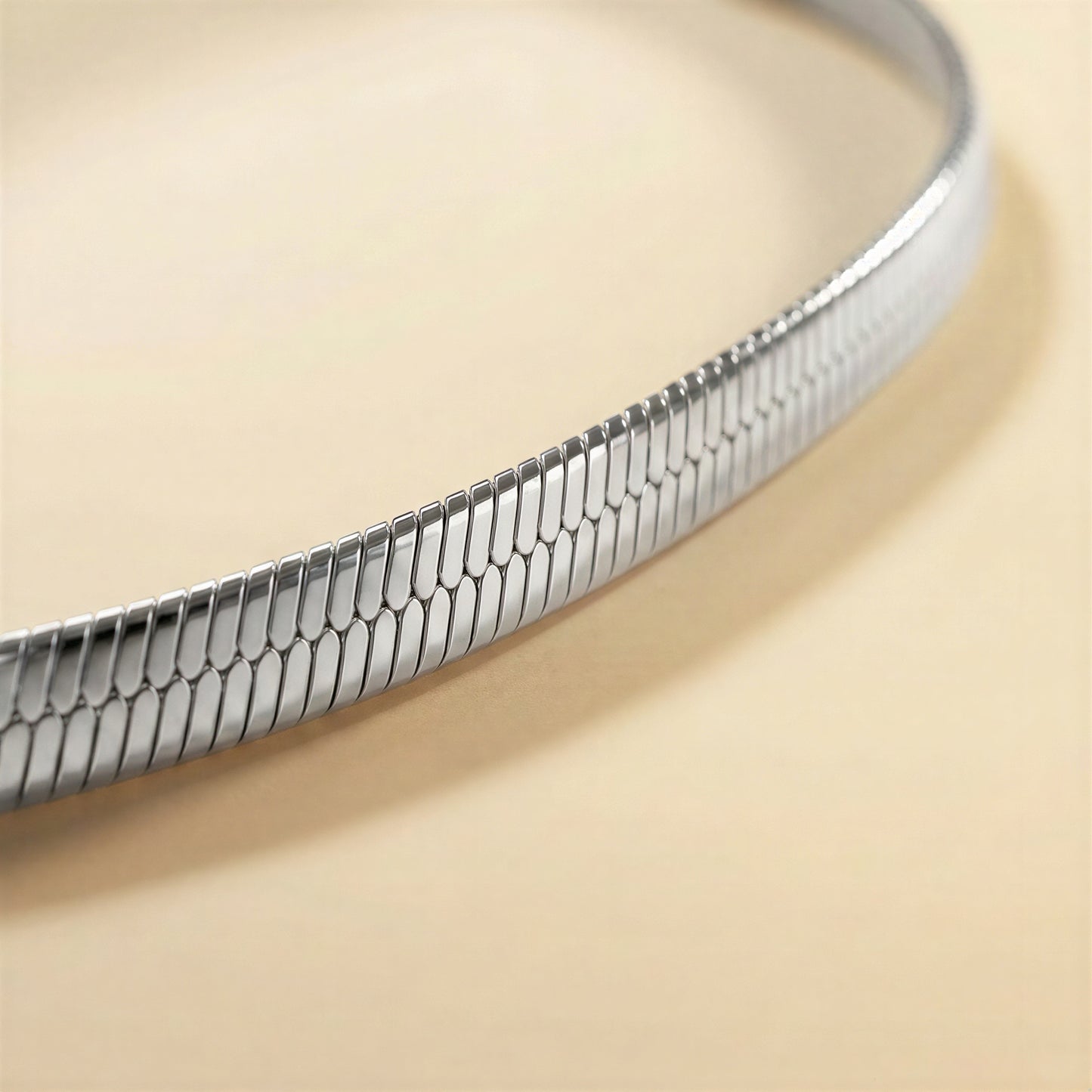 A close-up of a silver snake skin chain bracelet on a warm beige background.