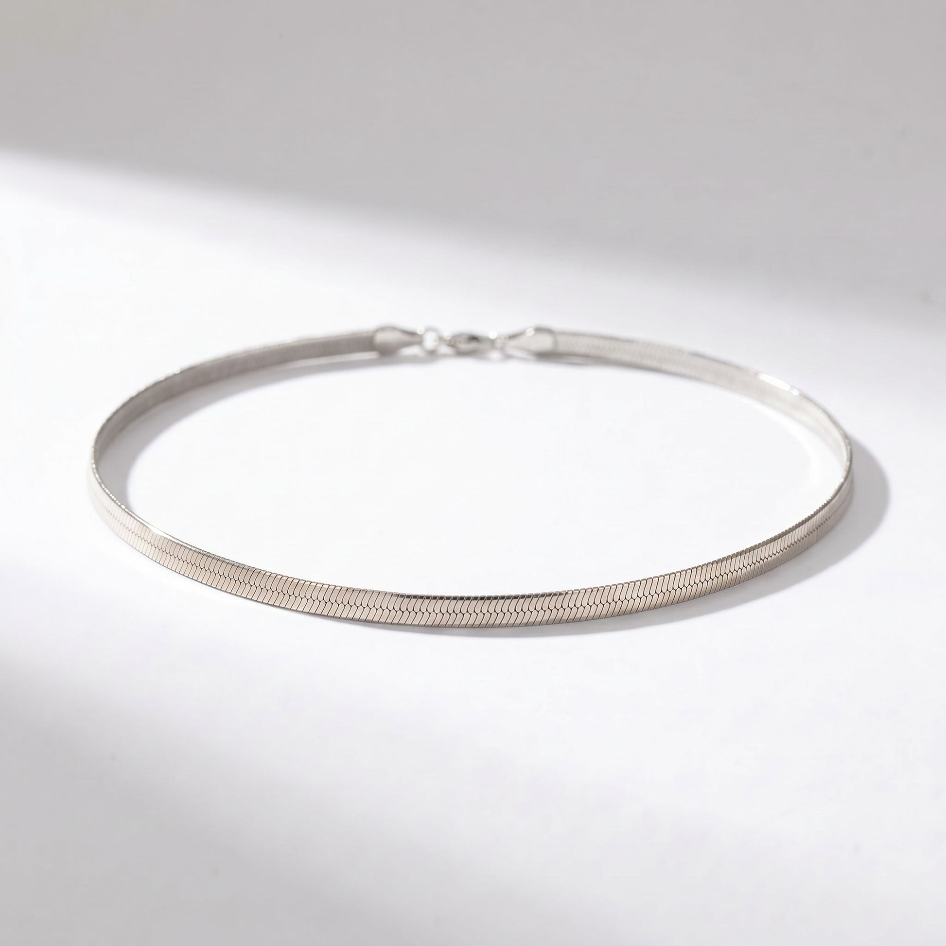 A thin silver snake chain bracelet with a textured finish and a lobster clasp, displayed on a clean white surface with soft shadows.