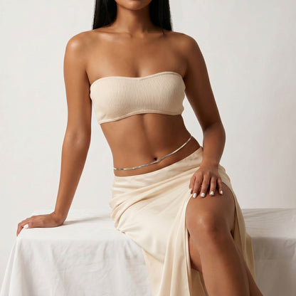 A woman models a ribbed beige tube top and a matching beige wrap skirt with a silver chain waist accessory, posed against a neutral light background.