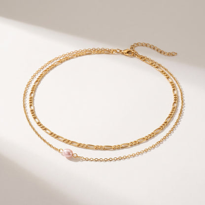 A delicate gold-toned double-layer necklace featuring a small pink freshwater pearl accent, displayed on a clean white surface with soft shadows.