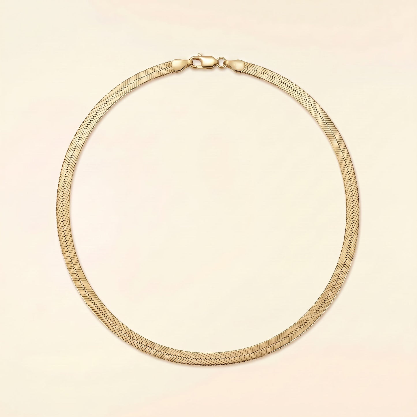 A gold-toned metal snake chain necklace with a lobster clasp, displayed in a circular shape against a solid pale pink background.