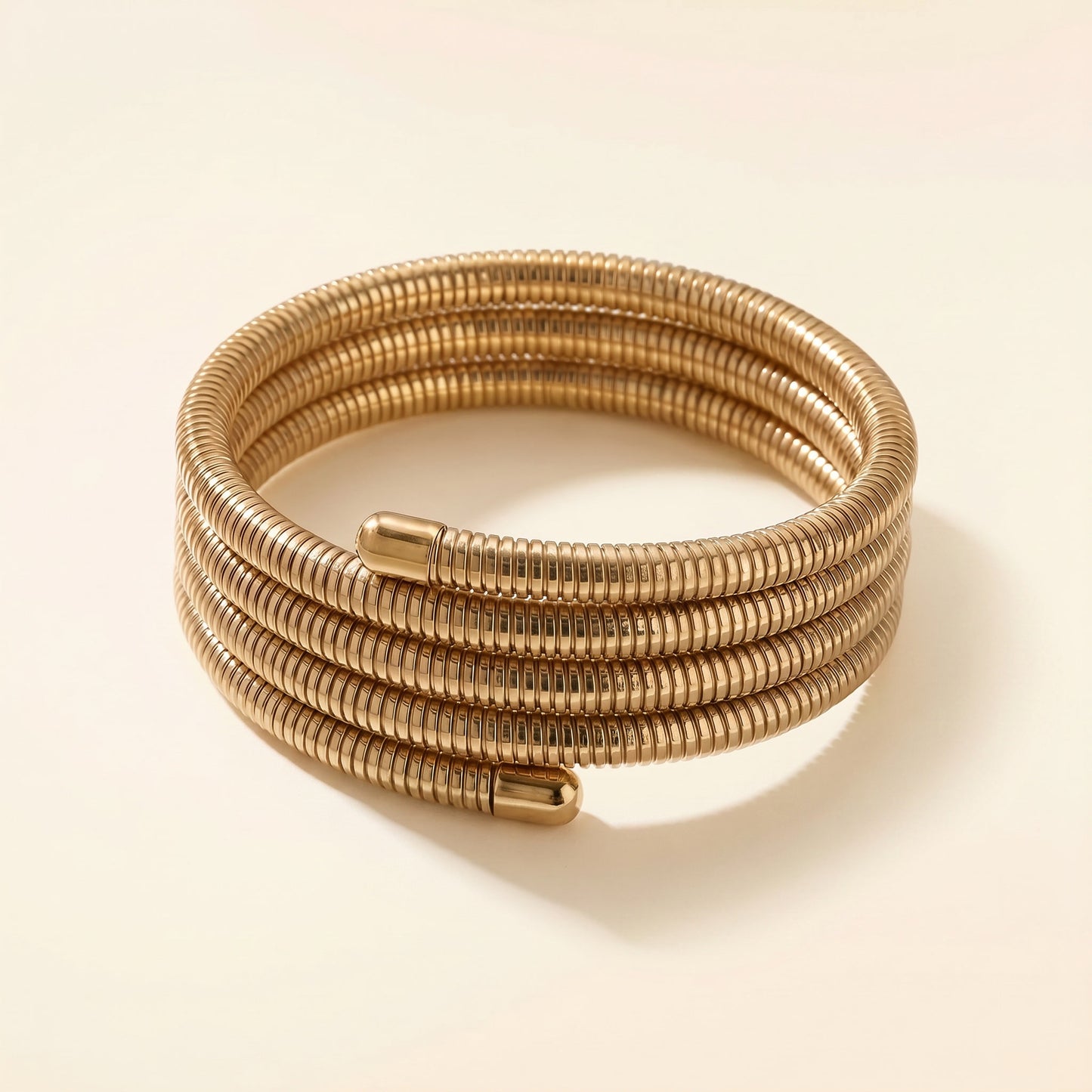 A coiled gold-toned metal bracelet with a textured, ribbed surface and a small cylindrical clasp, photographed on a clean cream background.