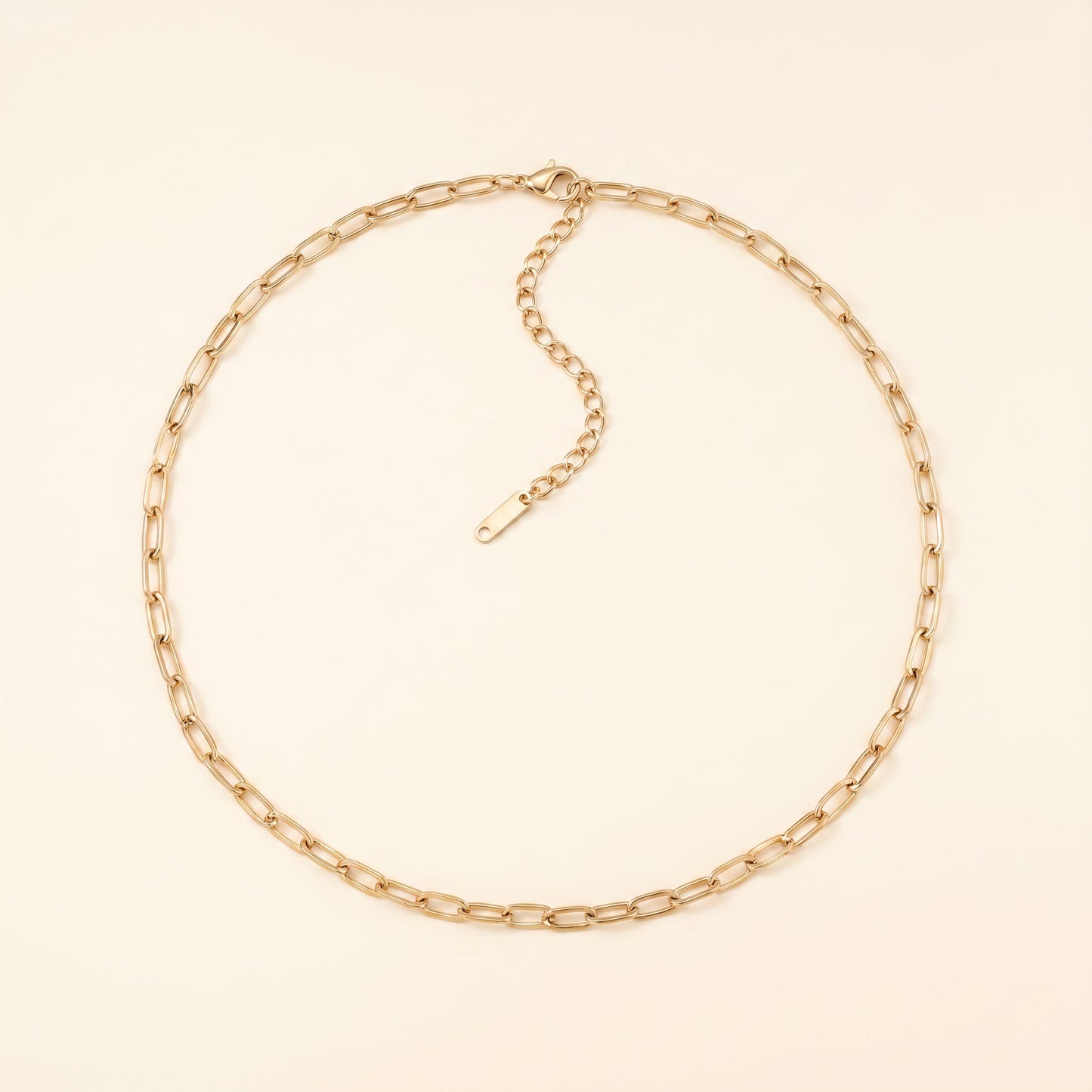 A gold paperclip chain necklace with an adjustable extender chain and clasp, displayed on a light cream background.