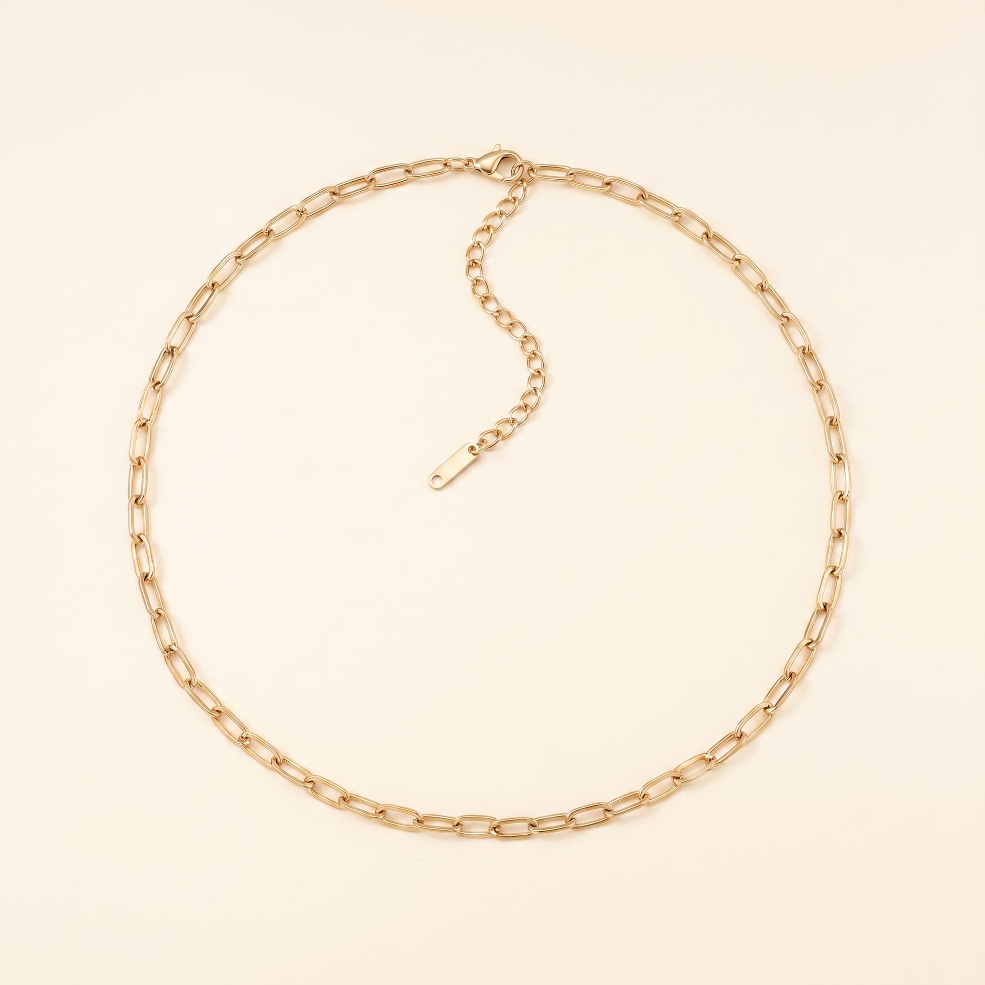 A gold paperclip chain necklace with an adjustable extender chain and clasp, displayed on a light cream background.