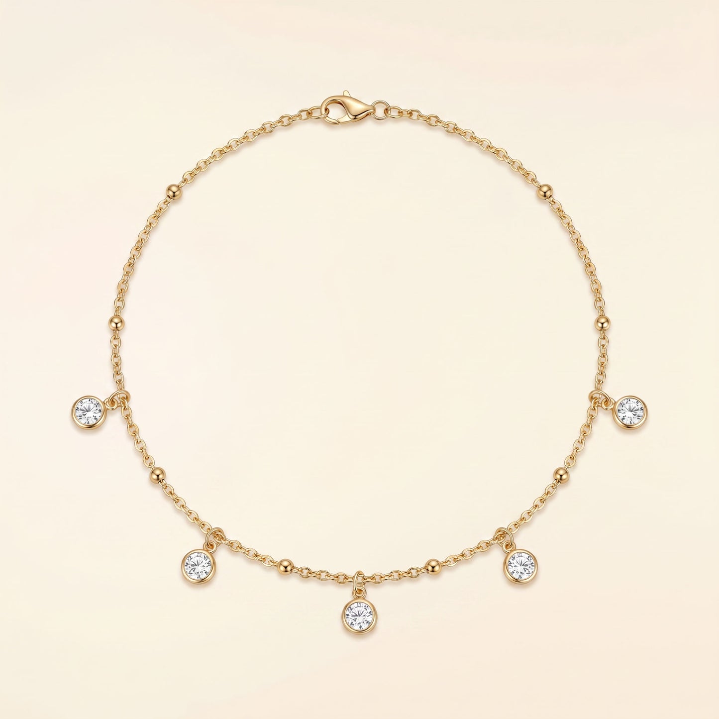 A delicate gold chain necklace with five small clear gemstone charms and a lobster clasp, displayed on a soft cream background.