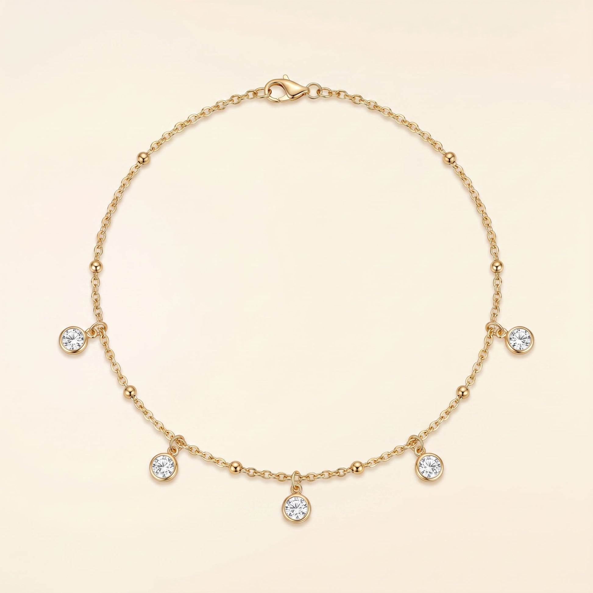 A delicate gold chain necklace with five small clear gemstone charms and a lobster clasp, displayed on a soft cream background.