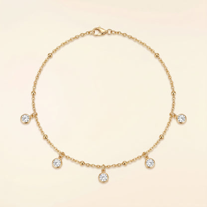 A delicate gold chain necklace with five small clear gemstone charms and a lobster clasp, displayed on a soft cream background.