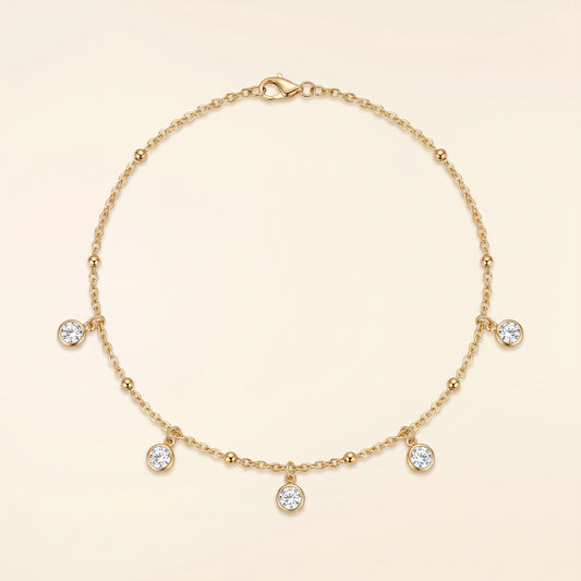 A delicate gold chain necklace with five small clear gemstone charms and a lobster clasp, displayed on a soft cream background.