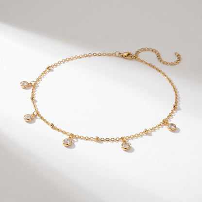 A delicate gold chain necklace with five small clear gemstone charms, displayed on a clean white background with soft shadows.