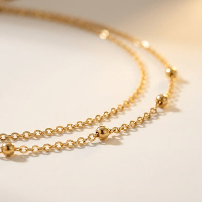 A close-up of a delicate gold chain necklace with small polished bead accents, photographed on a soft off-white background.