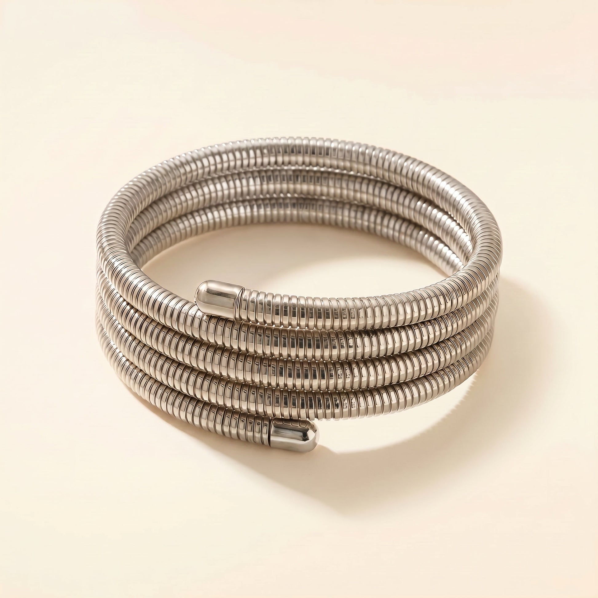 A coiled silver metal cable or hose with a ribbed corrugated texture, photographed on a plain warm beige background.