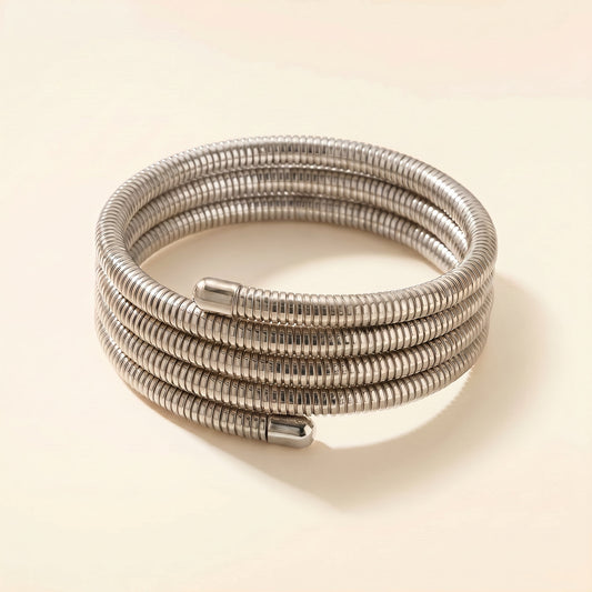 A coiled silver metal cable or hose with a ribbed corrugated texture, photographed on a plain warm beige background.