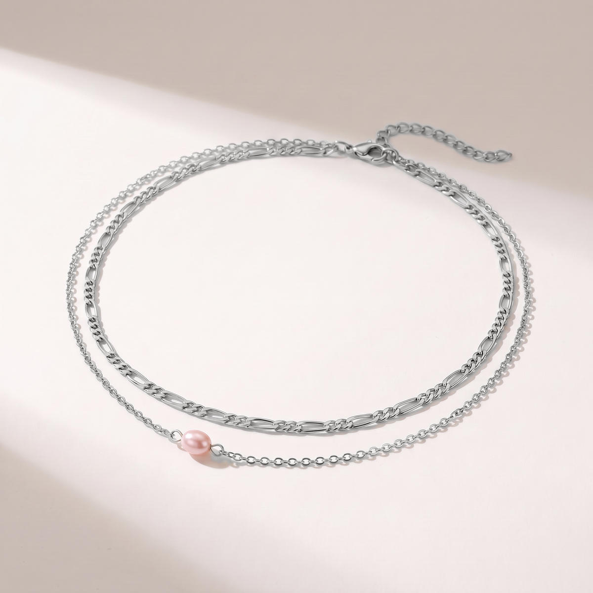 A delicate silver-toned double-layer necklace featuring a small pink freshwater pearl accent, displayed on a clean white surface with soft shadows.