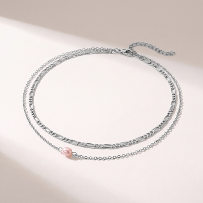A delicate silver-toned double-layer necklace featuring a small pink freshwater pearl accent, displayed on a clean white surface with soft shadows.