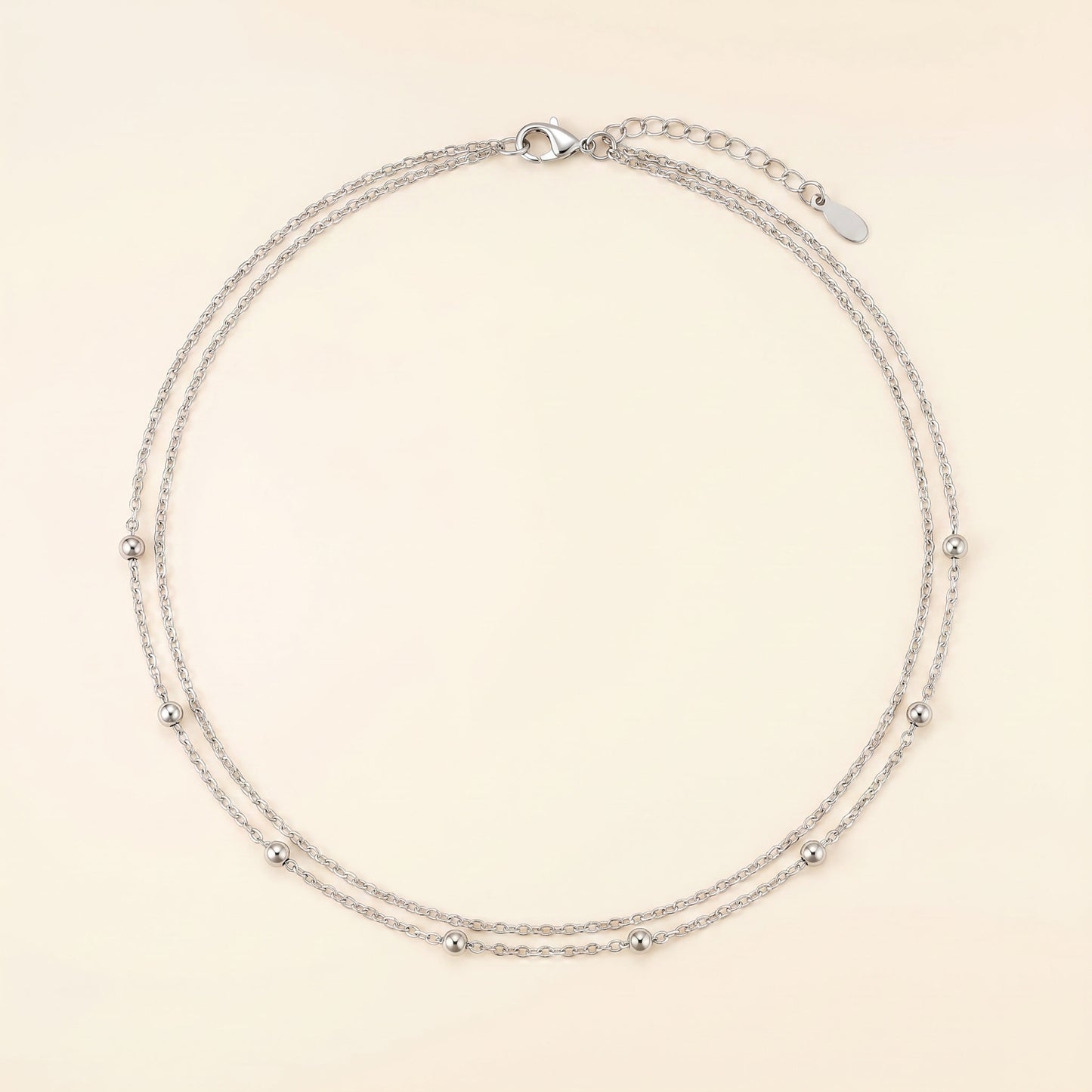A delicate silver double-strand chain necklace with small metallic beads spaced along the chain, displayed on a light cream background.
