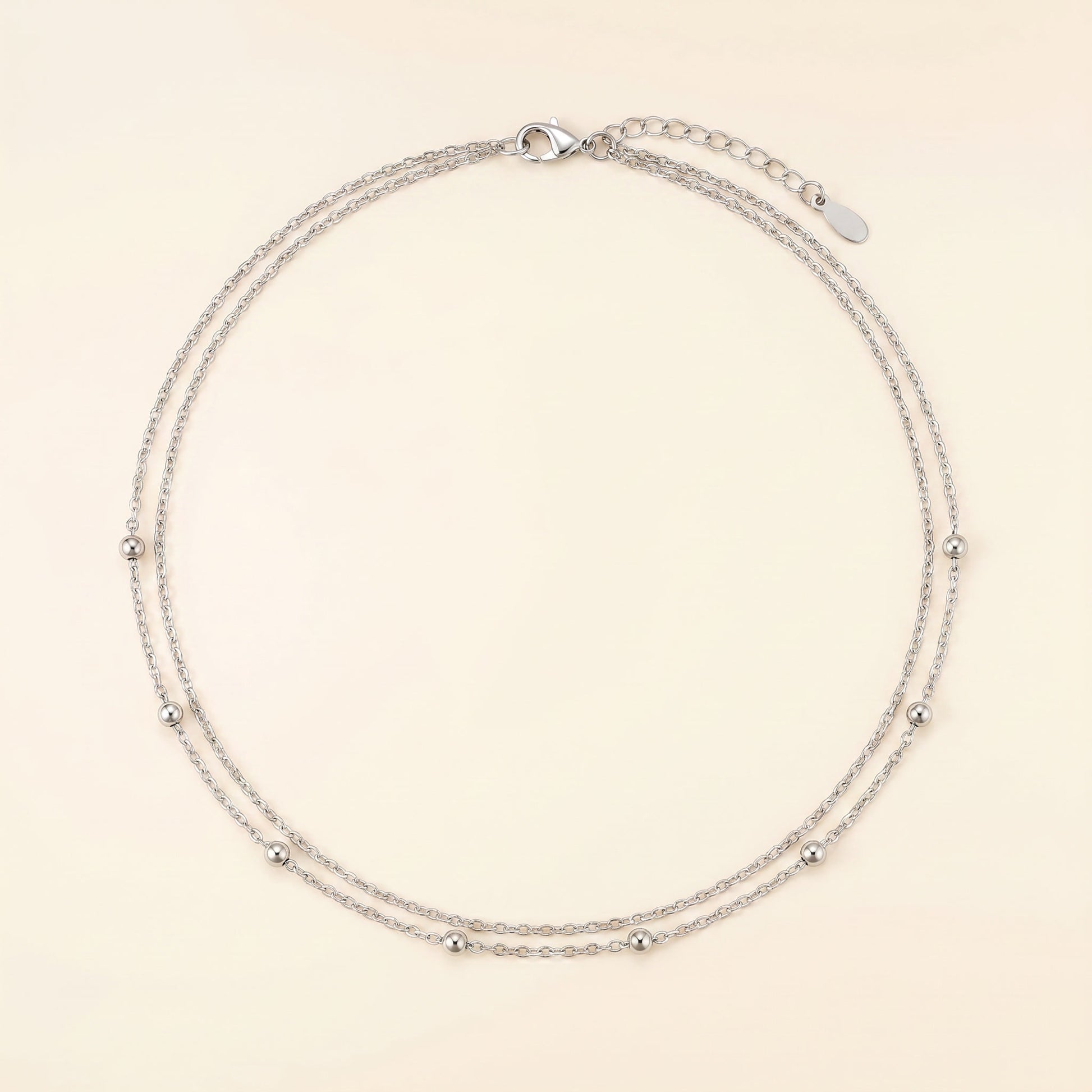 A delicate silver double-strand chain necklace with small metallic beads spaced along the chain, displayed on a light cream background.