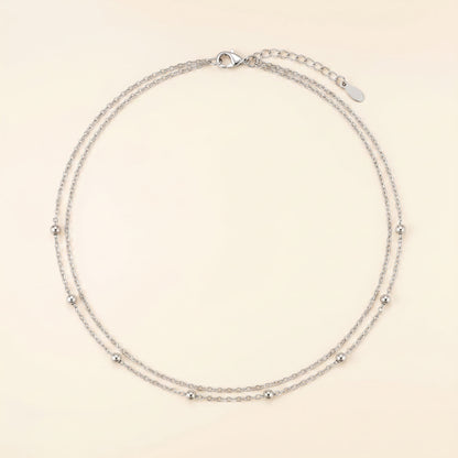 A delicate silver double-strand chain necklace with small metallic beads spaced along the chain, displayed on a light cream background.