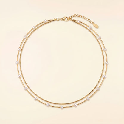 A double-strand gold chain necklace adorned with small white pearls, displayed on a light beige background.