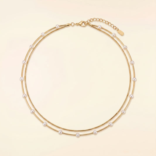 A double-strand gold chain necklace adorned with small white pearls, displayed on a light beige background.