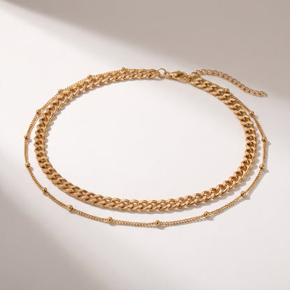 A double-layered gold chain necklace featuring a chunky curb chain and a delicate beaded chain, displayed on a clean white background with soft shadows.