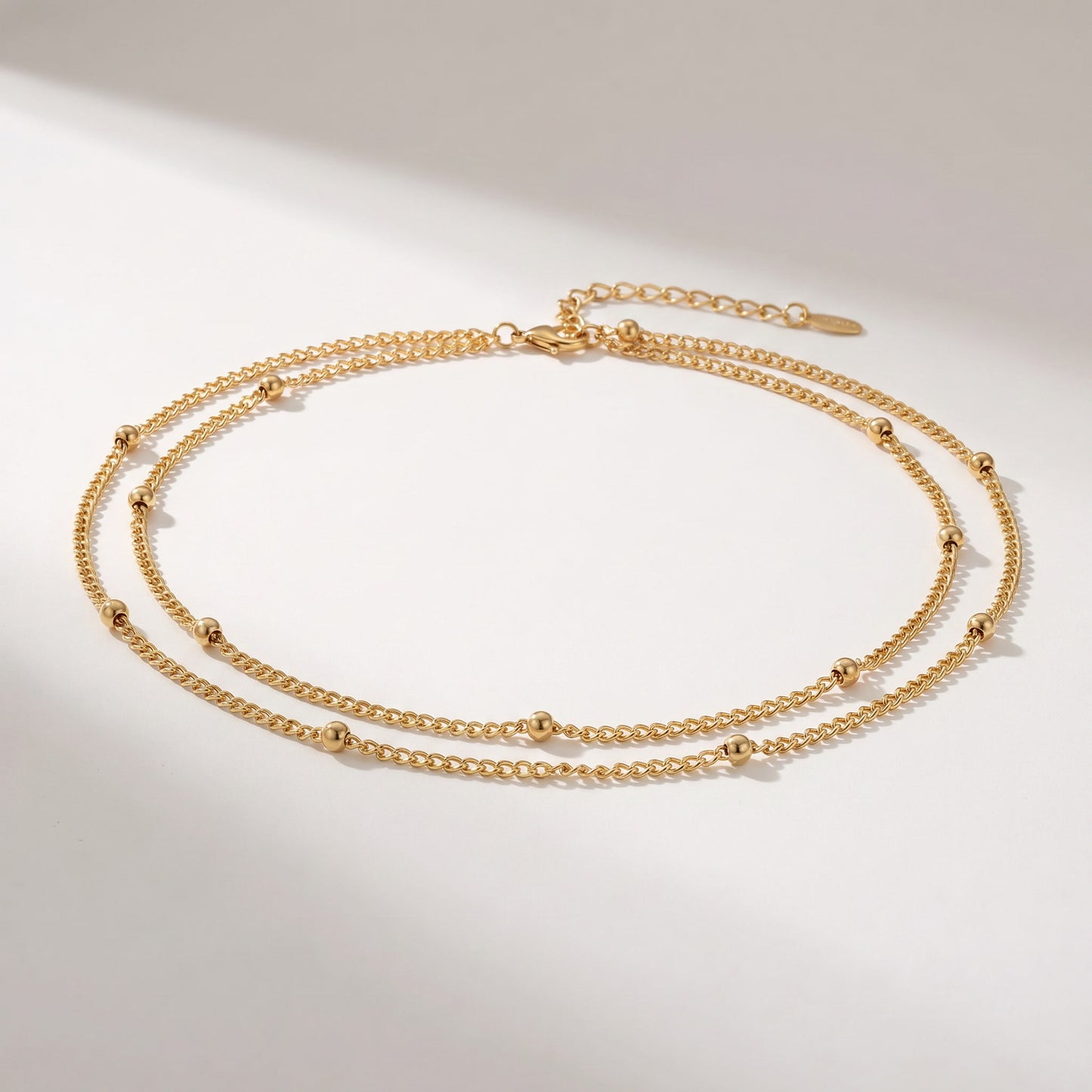 A delicate double-layered gold chain necklace with small bead accents, displayed on a clean white background with soft shadows.