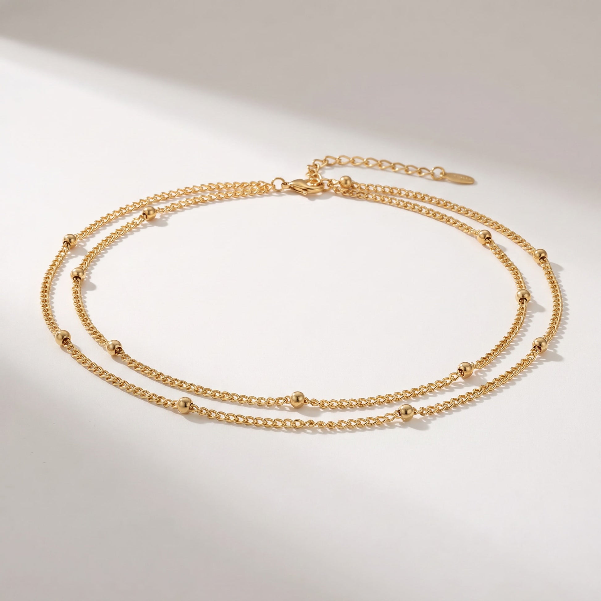 A delicate double-layered gold chain necklace with small bead accents, displayed on a clean white background with soft shadows.