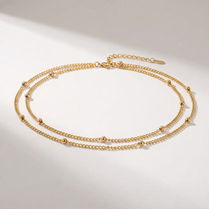 A delicate double-layered gold chain necklace with small bead accents, displayed on a clean white background with soft shadows.