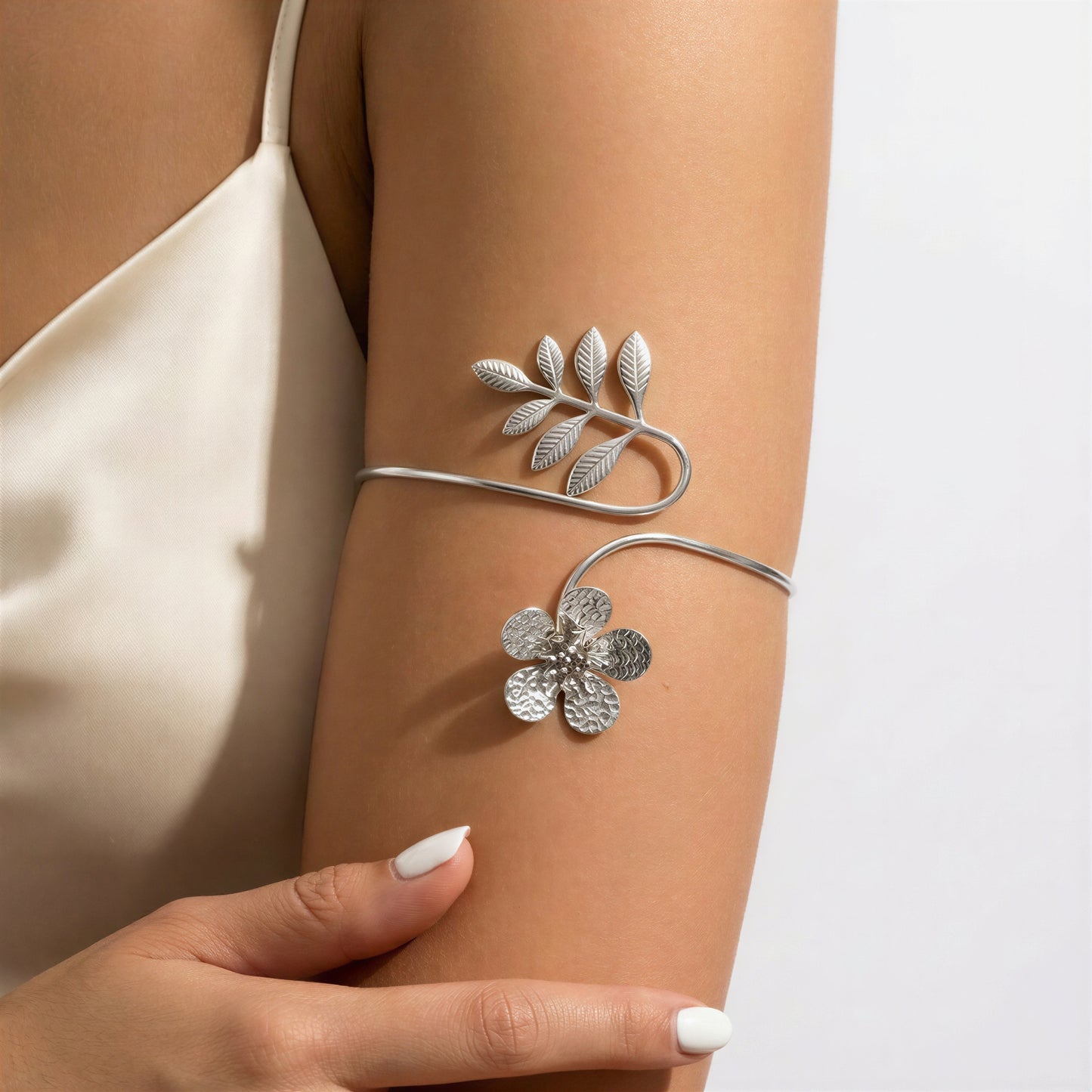 A silver-toned wrap bracelet with a leafy branch and flower motif, shown worn on a model's upper arm.
