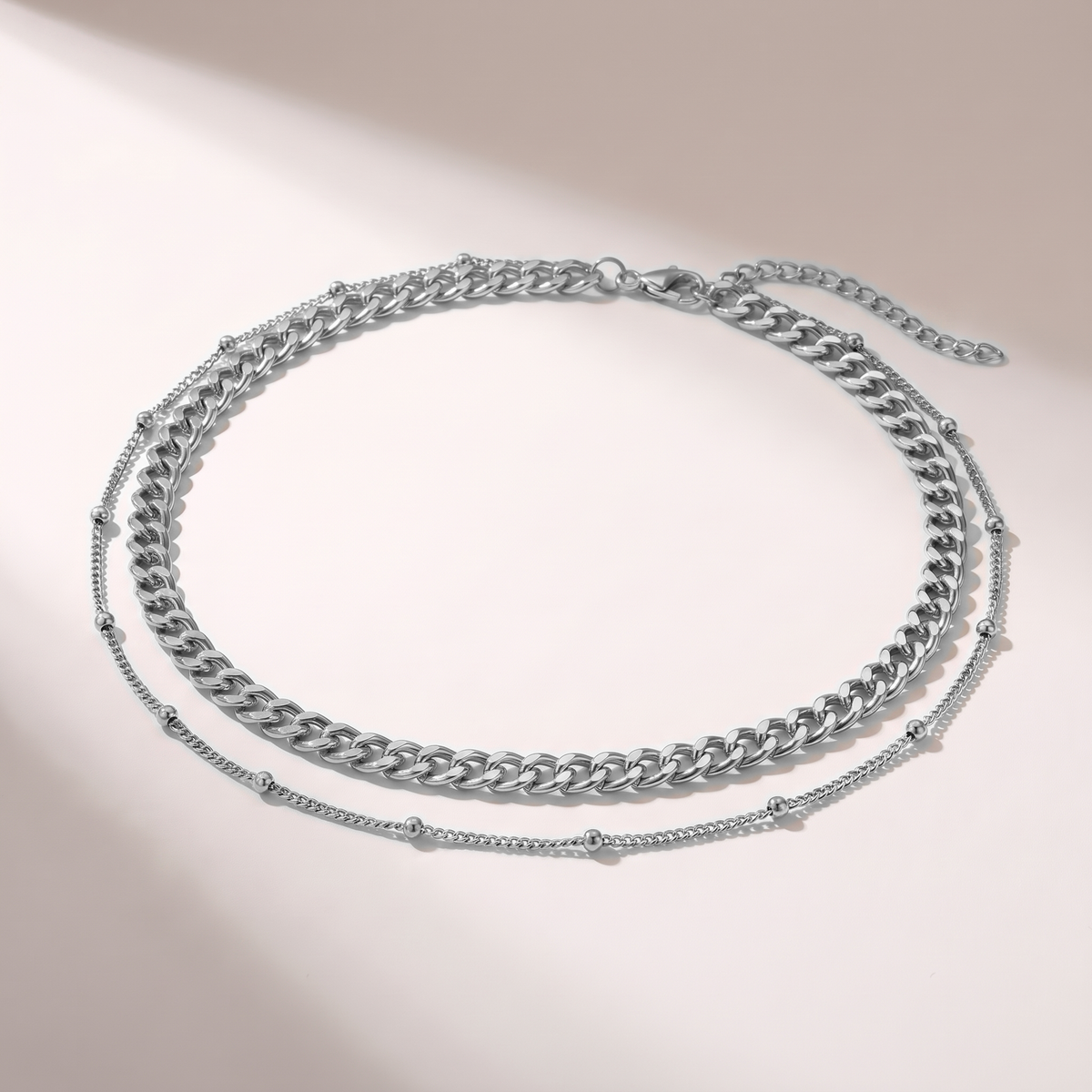 A double-layered silver chain necklace featuring a chunky curb chain and a delicate beaded chain, displayed on a clean white background with soft shadows.