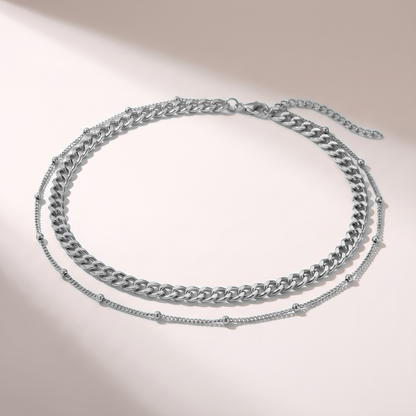 A double-layered silver chain necklace featuring a chunky curb chain and a delicate beaded chain, displayed on a clean white background with soft shadows.