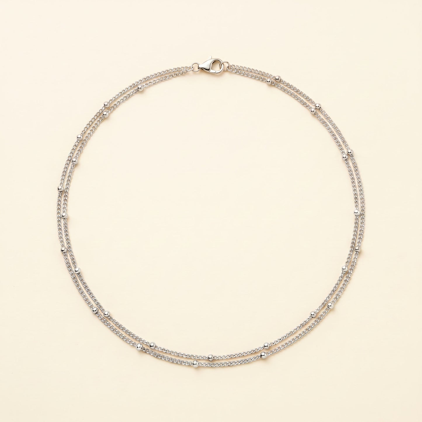 A delicate silver-toned double-strand necklace with small bead accents, displayed on a light cream background.