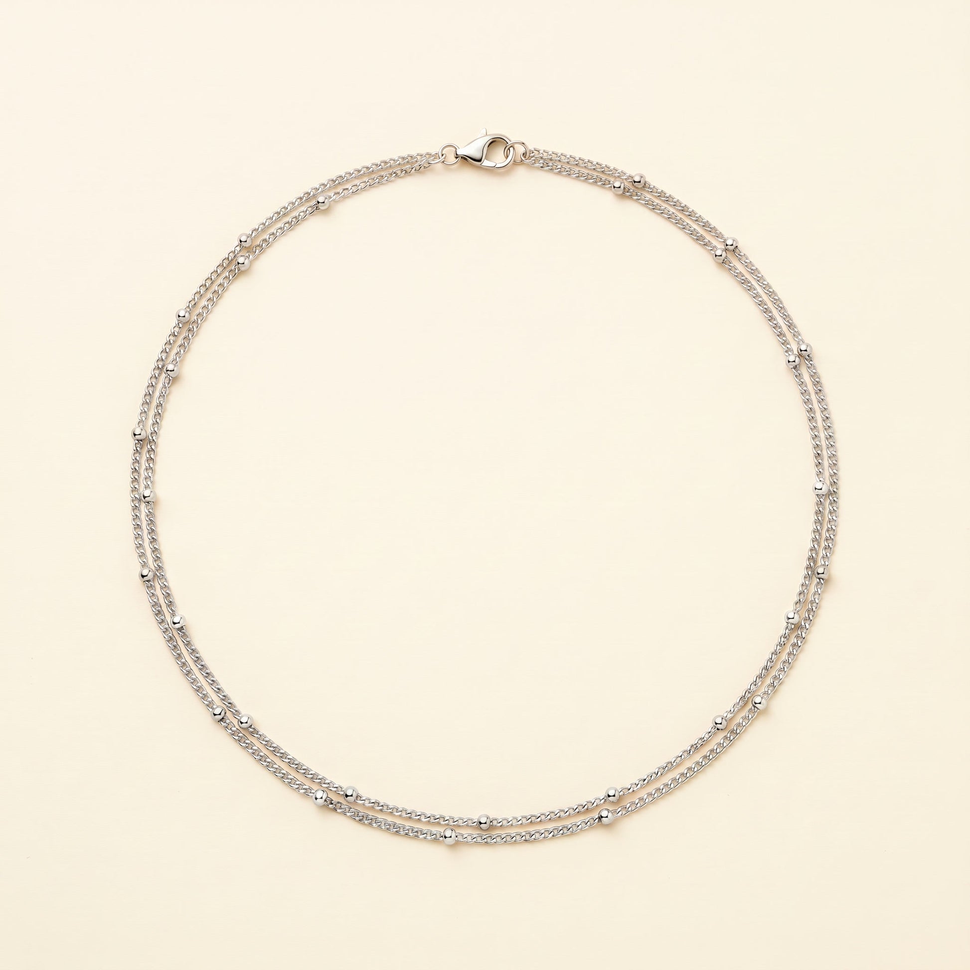 A delicate silver-toned double-strand necklace with small bead accents, displayed on a light cream background.