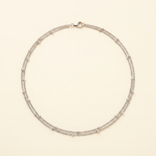 A delicate silver-toned double-strand necklace with small bead accents, displayed on a light cream background.