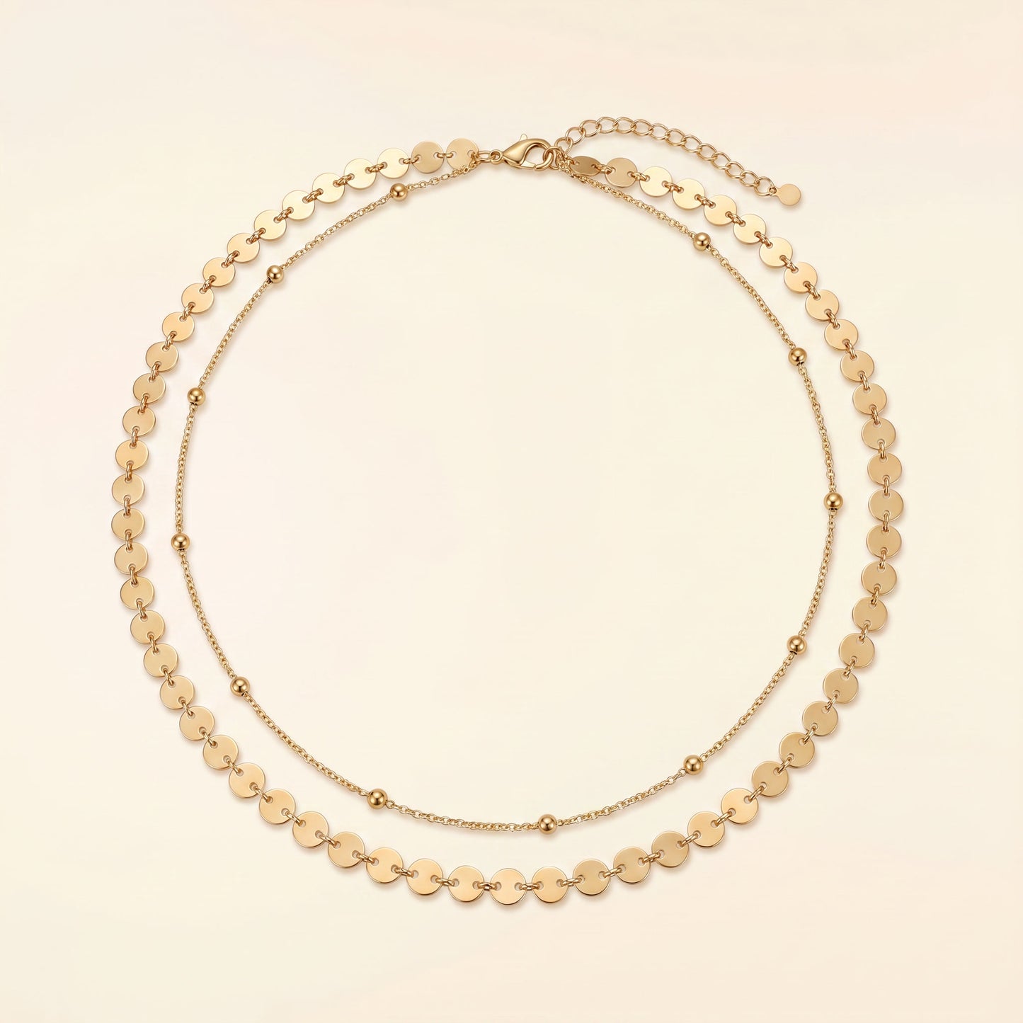 A gold-toned double-strand necklace featuring a layered design with flat circular disc links on the outer layer and smaller bead links on the inner layer, displayed on a light cream background.