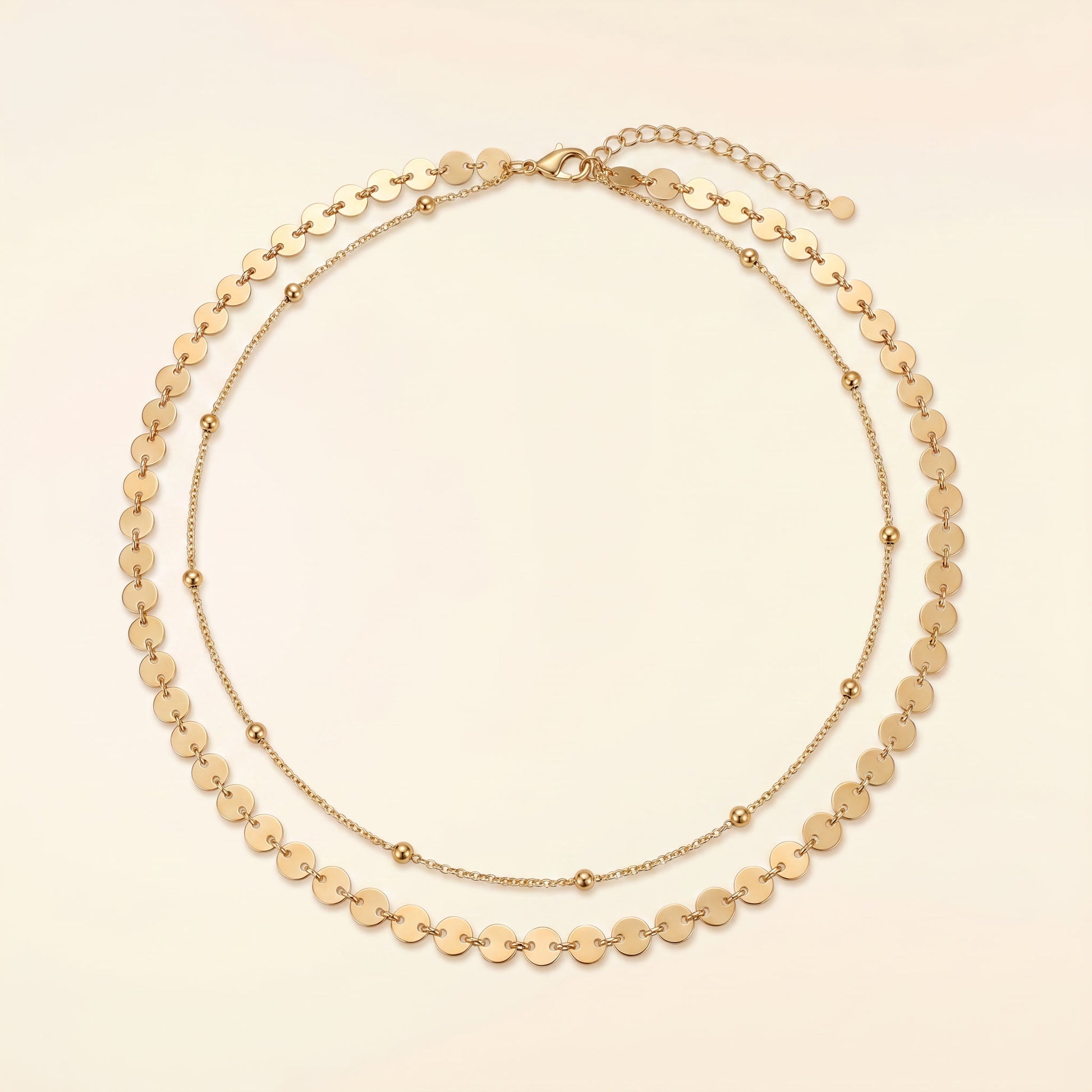 A gold-toned double-strand necklace featuring a layered design with flat circular disc links on the outer layer and smaller bead links on the inner layer, displayed on a light cream background.