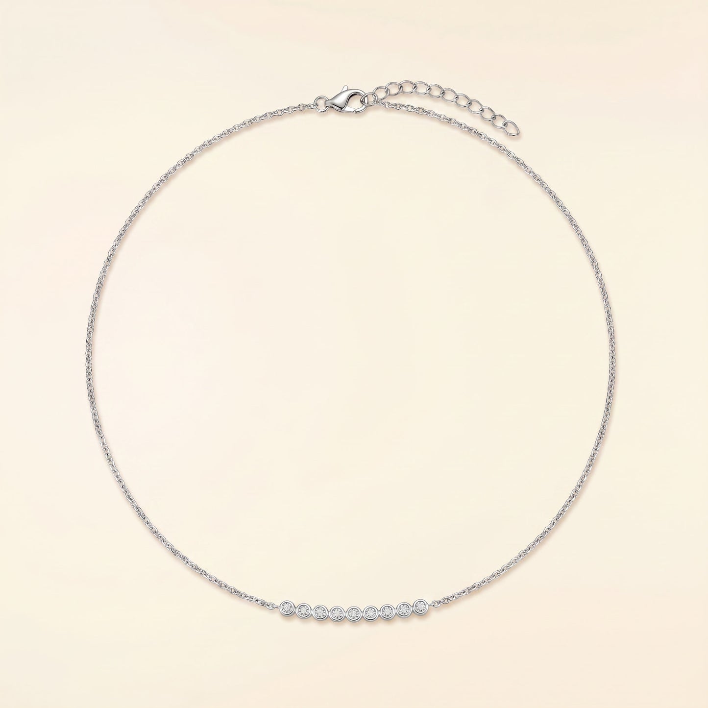 A delicate silver chain necklace with a short row of small clear stones across the front, displayed on a light cream background.