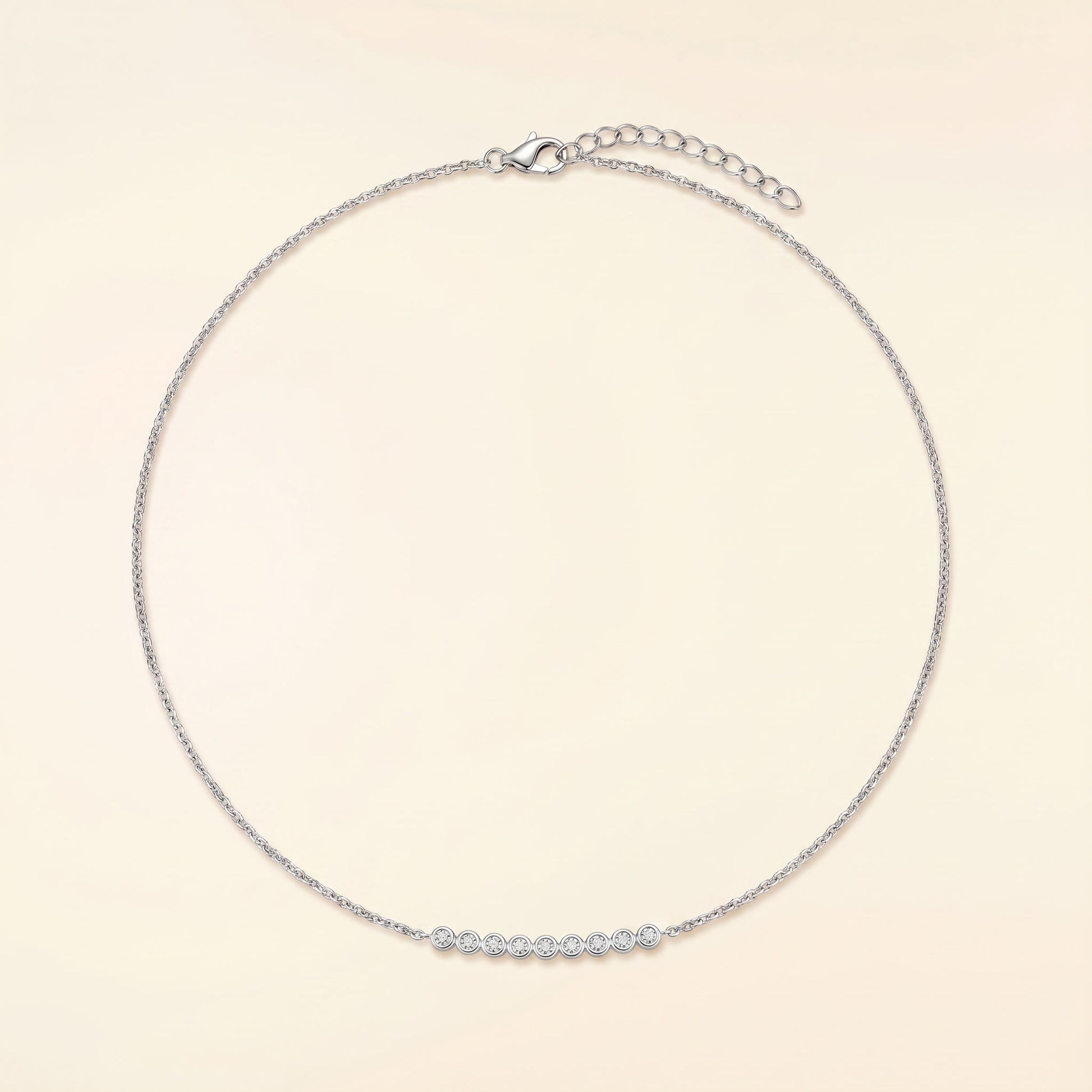 A delicate silver chain necklace with a short row of small clear stones across the front, displayed on a light cream background.