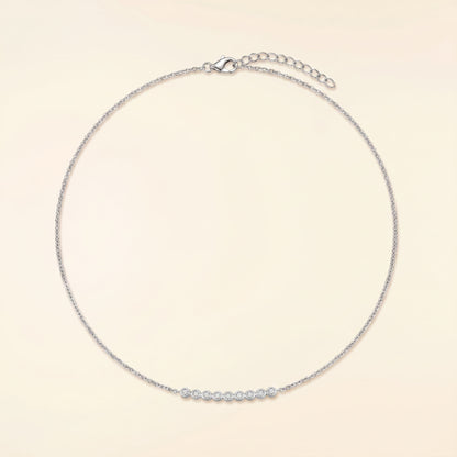 A delicate silver chain necklace with a short row of small clear stones across the front, displayed on a light cream background.
