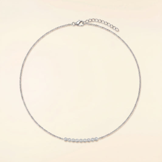 A delicate silver chain necklace with a short row of small clear stones across the front, displayed on a light cream background.
