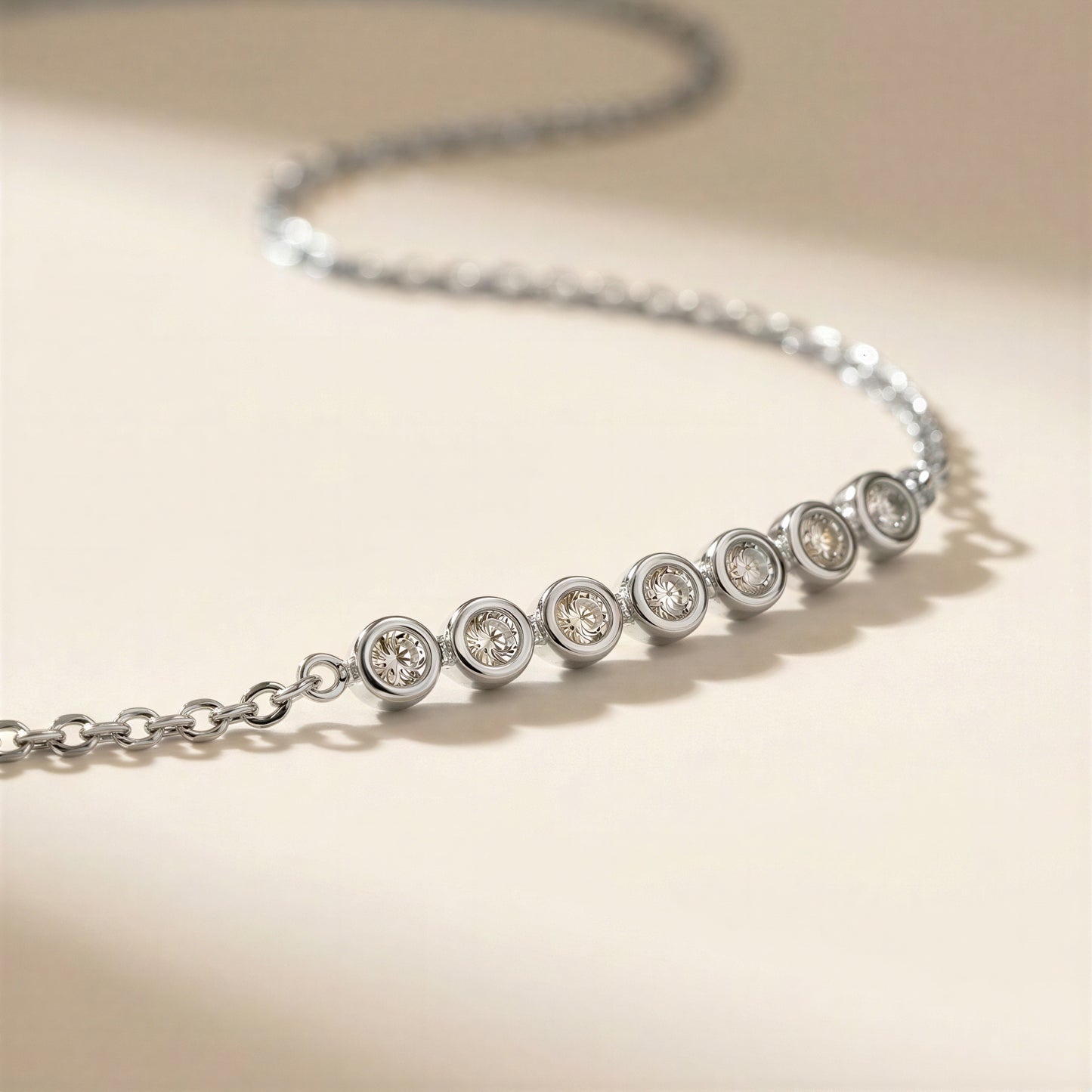 A silver chain necklace with seven bezel-set round clear stones, photographed on a warm beige background.