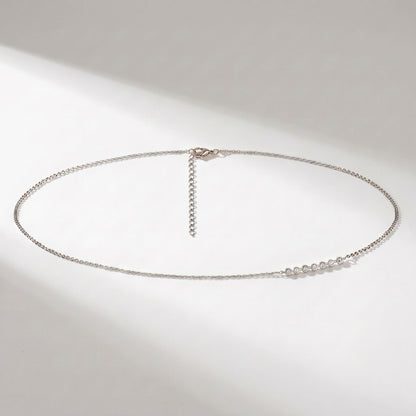 A delicate silver chain necklace with a small cluster of clear stones on one side and an adjustable hanging chain clasp, displayed on a light gray background with soft shadows.